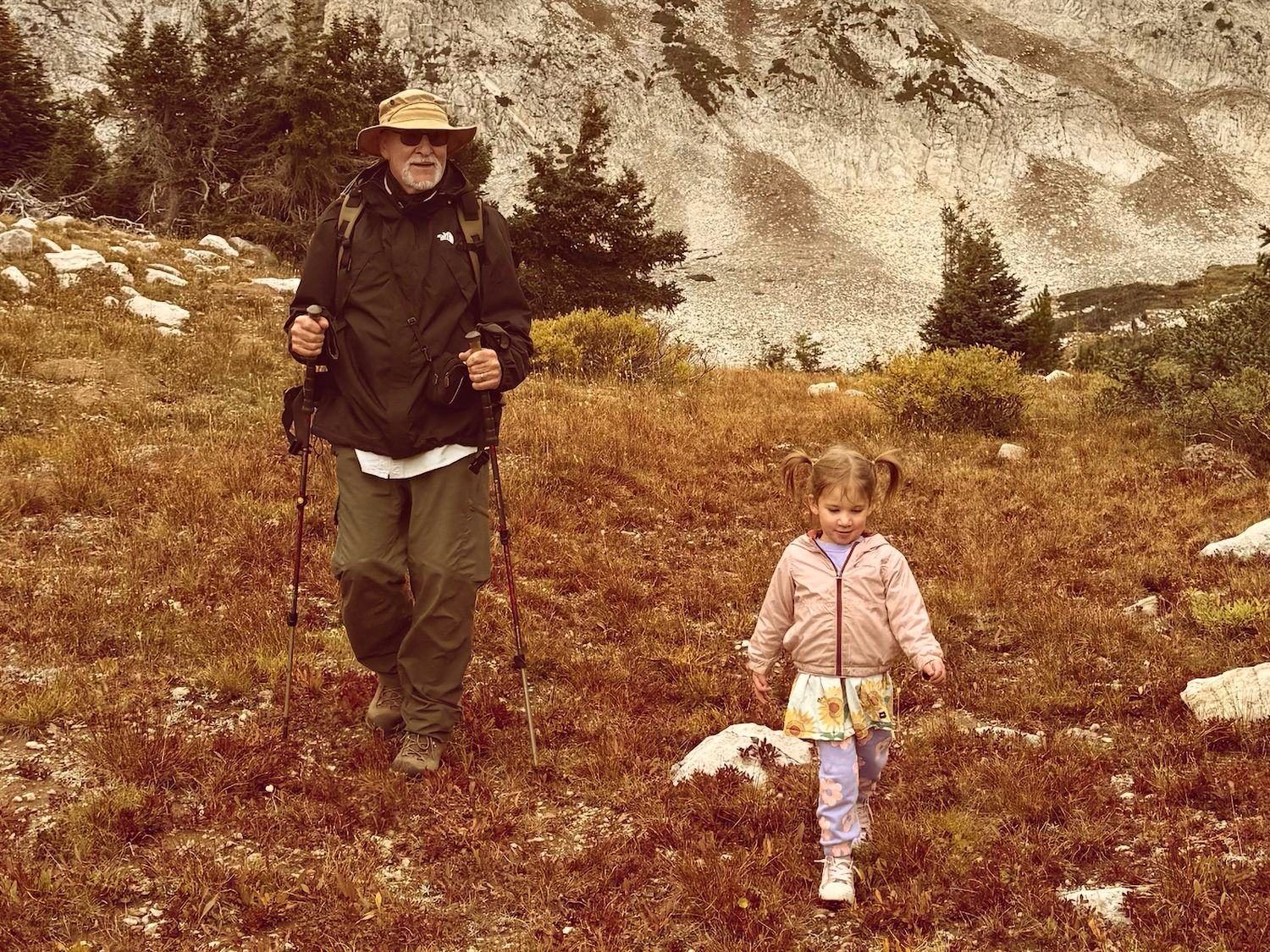 An older man walking a mountain trail with a small child
